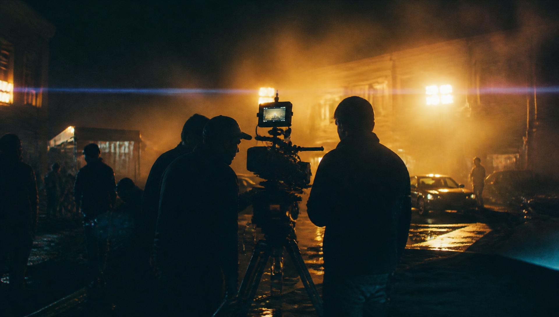 Film crew shooting a night exterior scene lit by warm tungsten lights